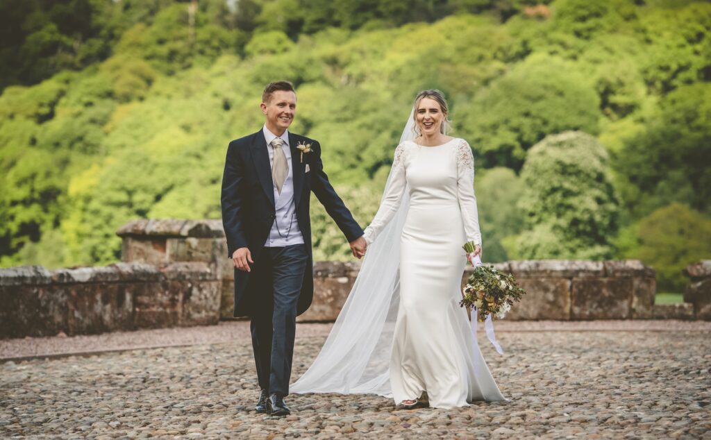 Newlyweds walking hand in hand across The Citadel's castle terrace overlooking the North Shropshire countryside